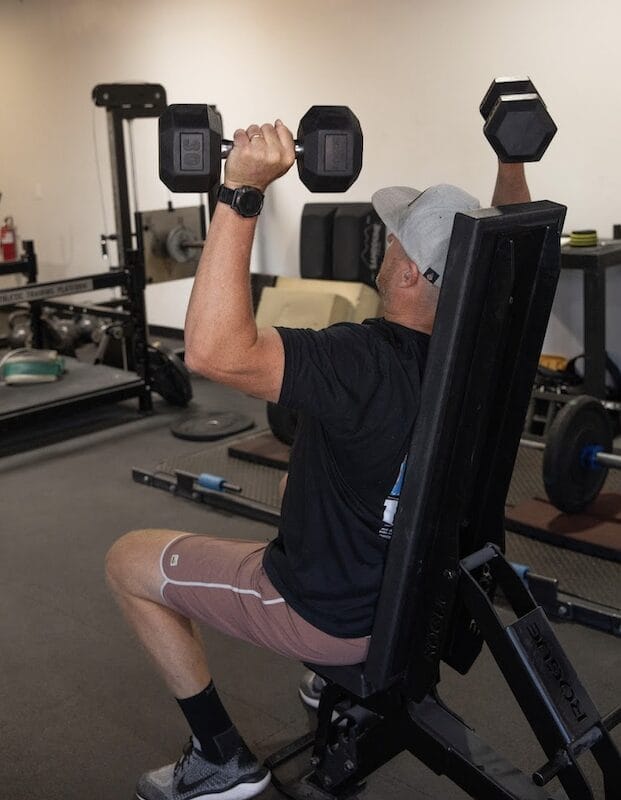  Man performing seated press using progressive overload method at Telos Strength in Tucson.
